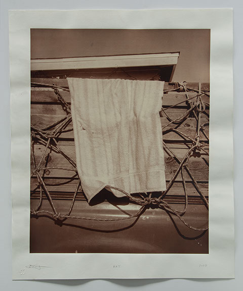 Photo of towel hanging off side of pickup truck on lumber tied using a netting of rope. Eave of roof from next door seems to sit on top of cargo