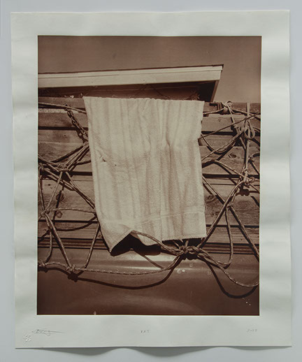 Photo of towel hanging off side of pickup truck on lumber tied using a netting of rope. Eave of roof from next door seems to sit on top of cargo