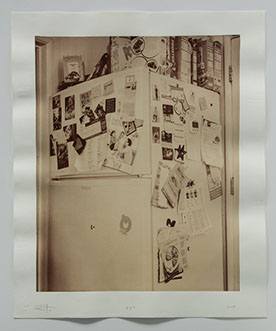 photo of refrigerator tucked in corner between door ways. covered with photos, notes and other personal momentos. Cereal boxes on top.
