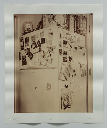 photo of refrigerator tucked in corner between door ways. covered with photos, notes and other personal momentos. Cereal boxes on top.