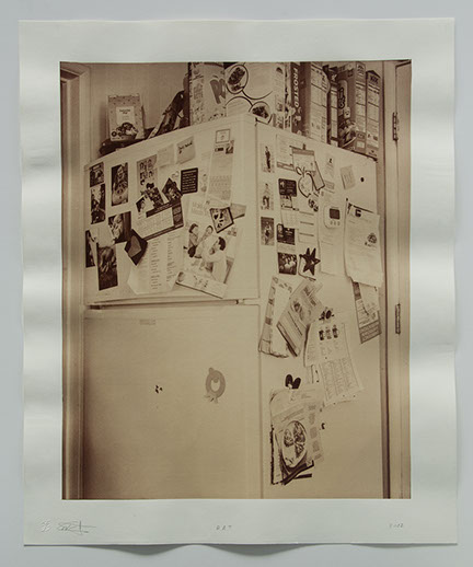 photo of refrigerator tucked in corner between door ways. covered with photos, notes and other personal momentos. Cereal boxes on top.
