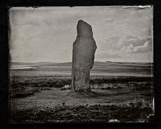 Panel B2-an ancient monolith center in the frame surrounded by swirls of grass, clouds & hills both shadowy & brightly lit. Low Horizon line.