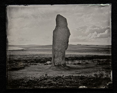 Panel B2-an ancient monolith center in the frame surrounded by swirls of grass, clouds & hills both shadowy & brightly lit. Low Horizon line.